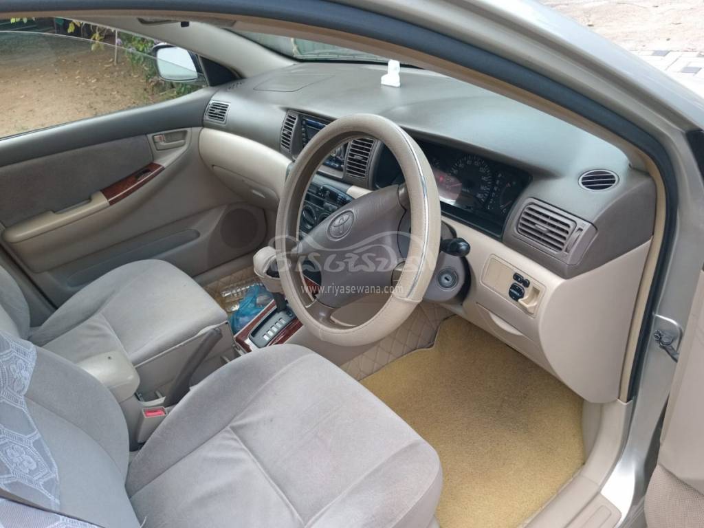 The interior view of the Toyota Corolla 121 G-grade JDM vehicle that clearly shows the steering wheel, gear lever, handbrake lever, Touch AC controls, Four AC louvers, Several storage compartments, and the passenger door with its armrest and the door bin.